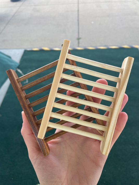 Hand holding a small wooden soap tray against a plain background