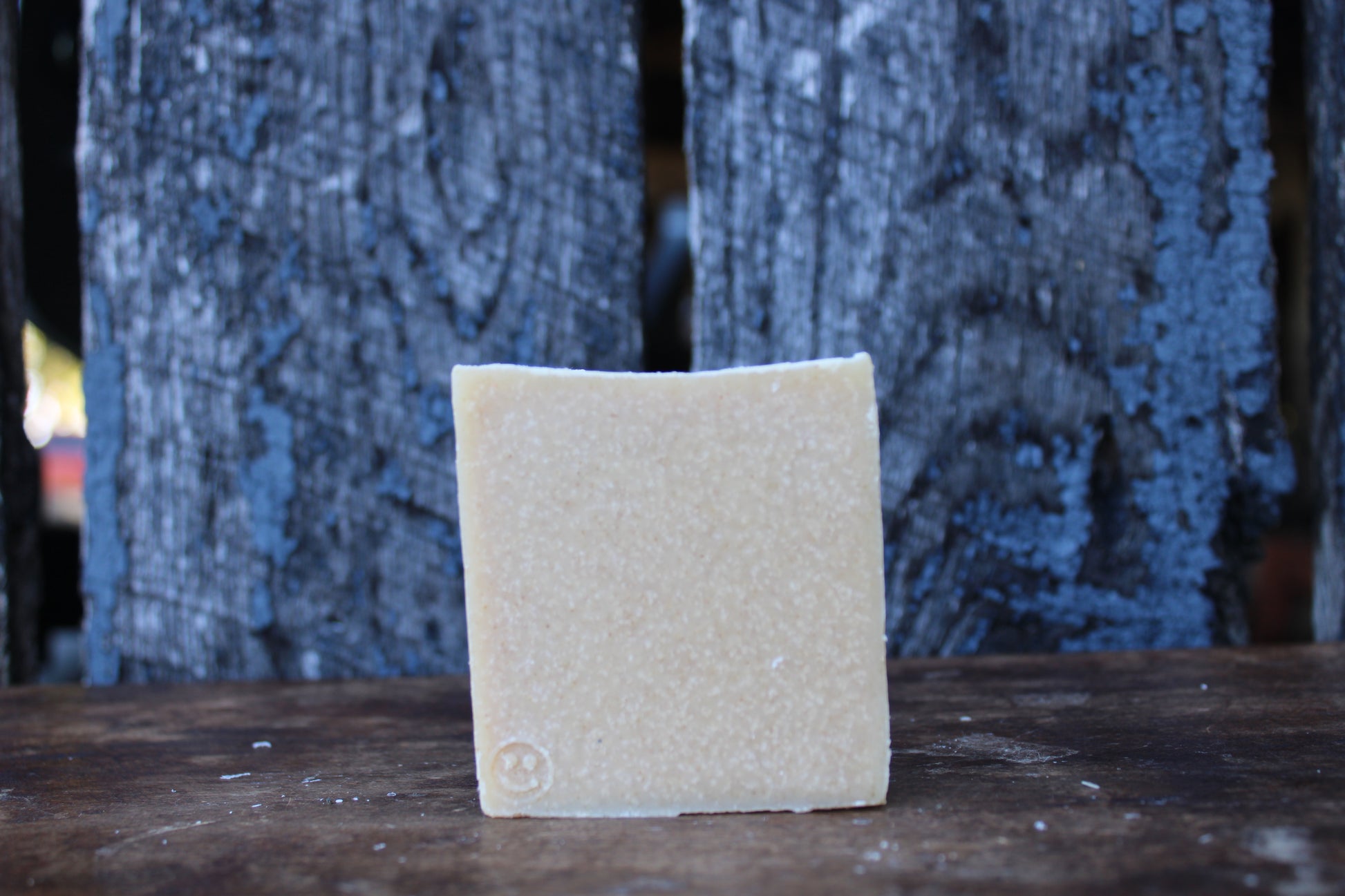 Square piece of beige soap on a wooden surface with a textured blue background