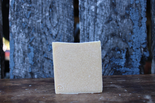 Square piece of beige soap on a wooden surface with a textured blue background