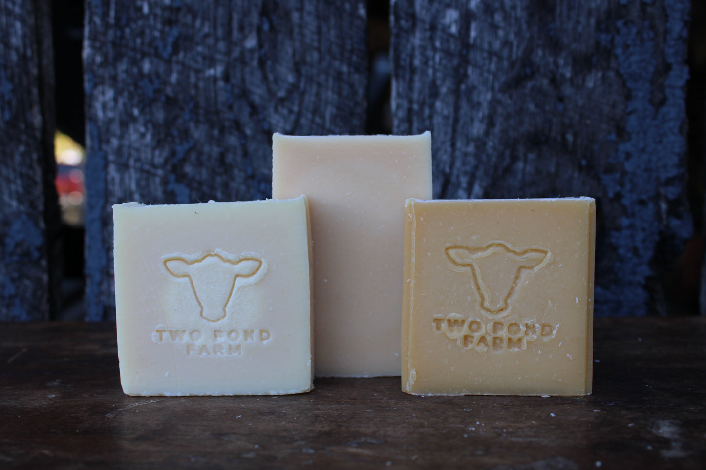 Three bars of soap from Two Pond Farm on a dark surface with a textured blue background