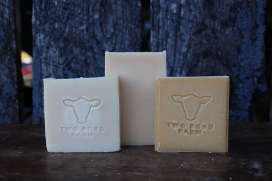 Three bars of soap from Two Pond Farm on a dark surface with a textured blue background